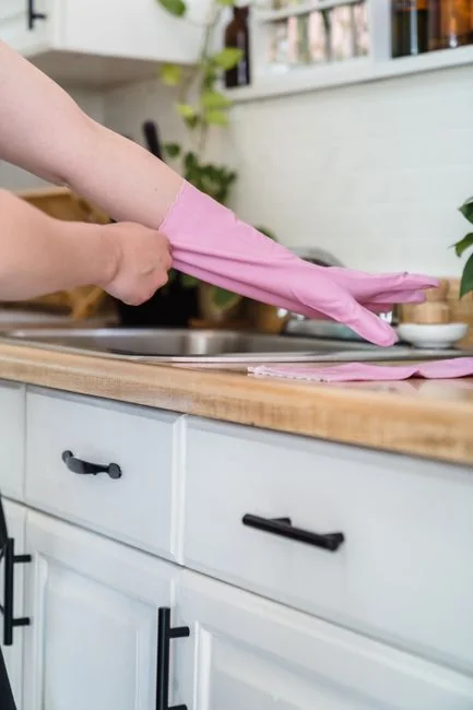 Un homme nettoie une paroi vitrée en extérieur avec une raclette, entouré de verdure.